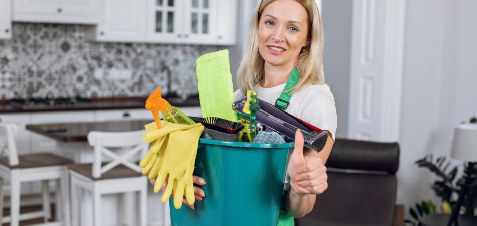 A woman with short hair and green shirt holding a bucket of cleaning supplies. A woman with short hair and green shirt holding a bucket of cleaning supplies.