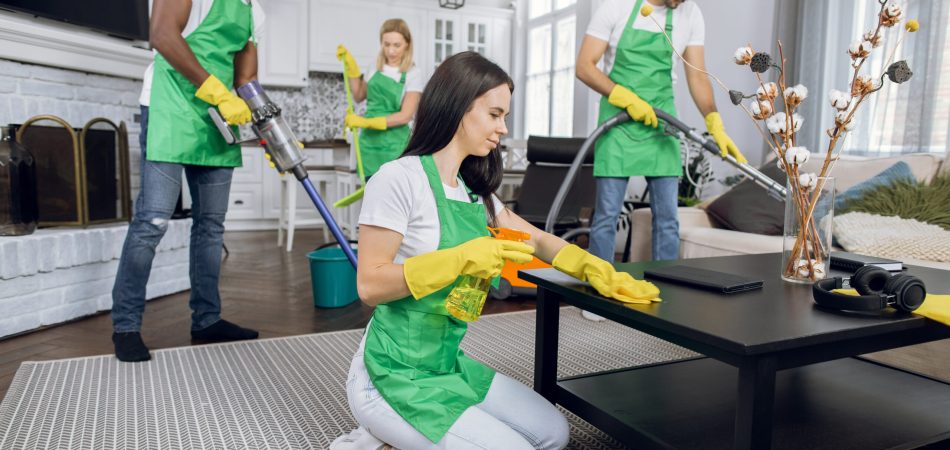 Two men and a woman in blue overalls cleaning a room and smiling into the camera