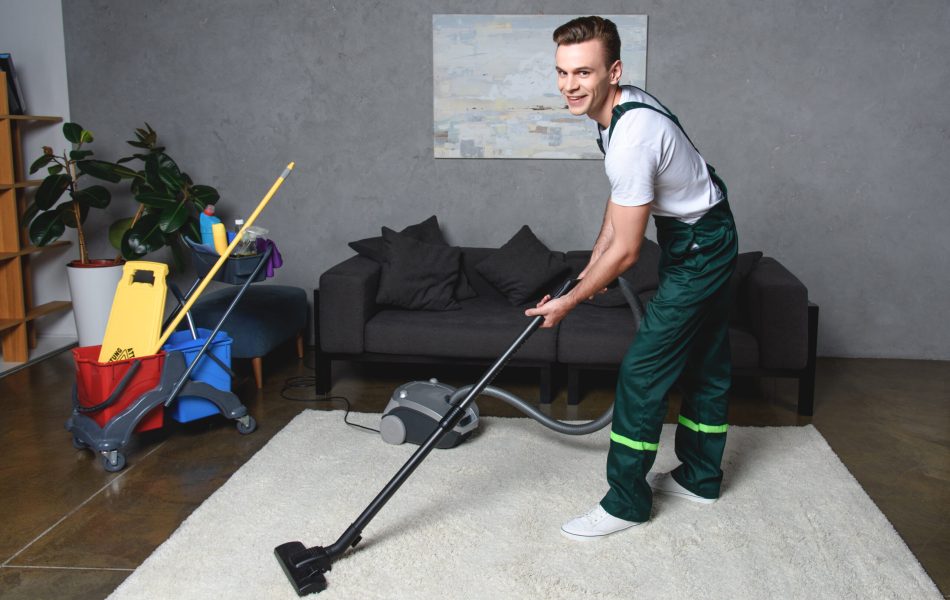 A young man in green overalls vacuuming a white carpet in a living room. A young man in green overalls vacuuming a white carpet in a living room.